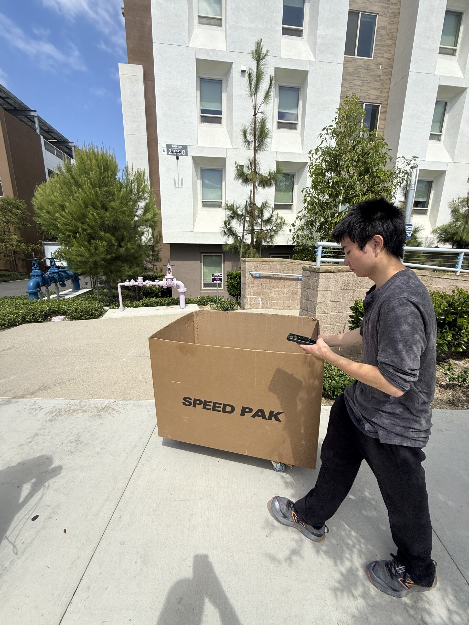 Person beside a rolling moving bin outside Plaza Verde apartments